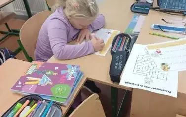 Dziewczynka siedzi w ławce szkolnej i rozwiązuje zadania