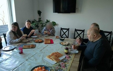 Osoby siedzą przy stole i jedzą gofry