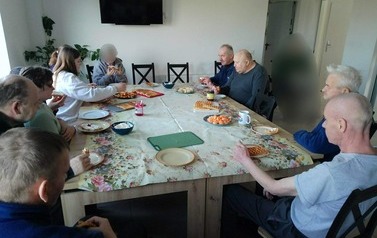 Osoby siedzą przy stole, jedzą gofry
