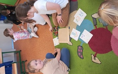 Dziewczynki siedzą na dywanie i grają w grę z kolorowymi kulkami