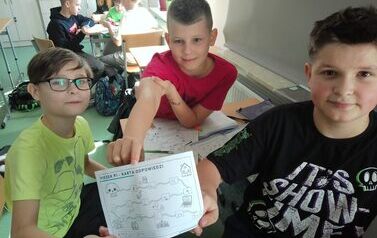 Uczniowie siedzą przy stolikach, rozwiązują zadania, prezentują kartę odpowiedzi.