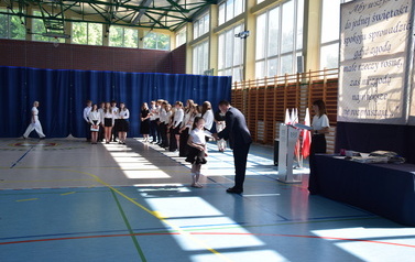 Dyrektor wręcza nagrodę dziewczynce, kt&oacute;ra uzyskała wysoki wynik w konkursie recytatorskim