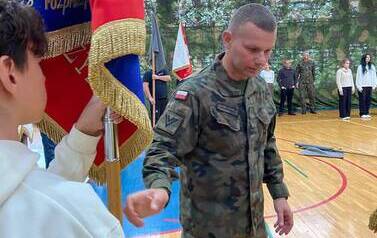 Żołnierz m&oacute;wi do chłopca, kt&oacute;ry trzyma sztandar