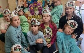 Dziewczynki z kl. II szkoły podstawowej pozują do zdjęcia na tle plakatu z napisem Dzień Ziemi. Uczennice ubrane są na kolorowo, na głowie mają opaski z rysunkiem Ziemi.