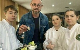 Troje uczni&oacute;w w białych fartuchach kucharskich, a pomiędzy nimi mężczyzna w okularach, jeansowej kurtce, trzymający kawałek sushi.