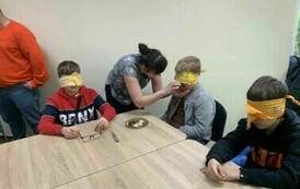 Trzech chłopc&oacute;w siedzi przy stole, mają zasłonięte oczy.