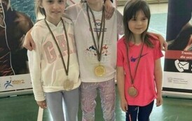 Trzy dziewczynki w strojach sportowych, stojące obok siebie, każda z nich ma medal przewieszony na szyi (złoto, srebro, brąz)