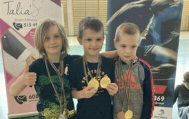 Trzech chłopc&oacute;w w strojach sportowych, stojących obok siebie, każdy z nich ma medal przewieszony na szyi