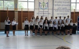 Uczniowie w biało-czarnych strojach ustawieni w dw&oacute;ch rzędach w trakcie akademii szkolnej