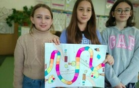 Trzy dziewczynki stojące obok siebie, trzymają przed sobą kartkę z narysowaną grą planszową