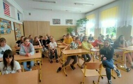 Uczniowie siedzą przy stolikach w sali lekcyjnej.