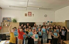 Liczna grupa uczni&oacute;w wraz z umundurowanymi mężczyznami pozuje do zdjęcia w sali lekcyjnej.
