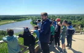 Grupa uczni&oacute;w wraz z przewodnikiem znajduje się na tarasie widokowym. Przed nimi rozciąga się widok rzeki i las&oacute;w.