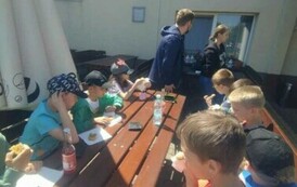 Uczniowie siedzą przy drewnianym stole, spożywają posiłek.