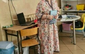Kobieta w sukience trzyma przed sobą książkę.