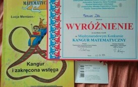 Na zdjęciu widnieje dyplom, książka oraz bilet do kina przyznane uczeniowi za wynik w konkursie Kangur Matematyczny