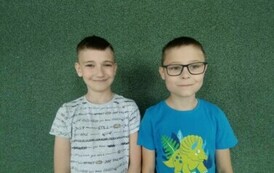 Dw&oacute;ch chłopc&oacute;w w koszulkach z kt&oacute;rkim rękawem pozują do zdjęcia na tle zielonej ściany.