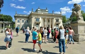 Rozproszeni uczestnicy wycieczki patrzą na Pałac na Wyspie w Łazienkach Kr&oacute;lewskich.