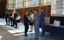 Uczeń klasy &oacute;smej odbiera świadectwo ukończenia szkoły podstawowej od dyrektora podczas uroczystego zakończenia roku szkolnego.