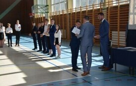Uczeń klasy &oacute;smej odbiera świadectwo ukończenia szkoły podstawowej od dyrektora plac&oacute;wki podczas uroczystego zakończenia roku szkolnego.