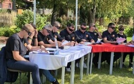 Grono lektor&oacute;w siedzi przy stole, w czarnych maskach, czyta Kordiana Juliusza Słowackiego.