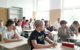Uczniowie siedzą przy stolikach w sali lekcyjnej.