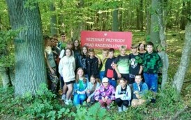 Grupa uczni&oacute;w pośr&oacute;d drzew przy tablicy informacyjnej.