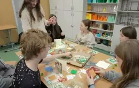 Uczniowie ozdabiają kartki świąteczne siedząc przy wsp&oacute;lnym stole.