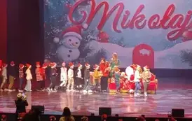 Na scenie Mikołaj wręcza prezenty dzieciom ustawionym w długim szeregu.