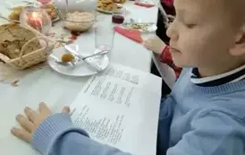Chłopiec siedzi przy stole wigilijnym, przed sobą ma kartkę z tekstem kolęd