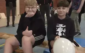 Dw&oacute;ch chłopc&oacute;w siedzi na ławce, jeden trzyma biały balon