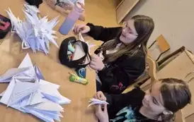 Dziewczynki siedzą przy stole i wycinają gwiazdki z gwiałego papieru