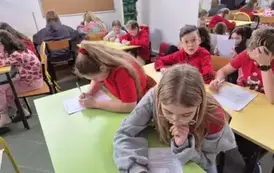 Uczniowie siedzą w ławkach szkolnych, piszą na kartkach