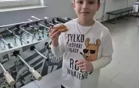 Chłopiec w białej koszulce z czarnymi napisami trzyma pączka