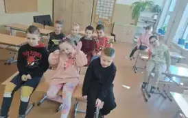 Uczniowie klasy pierwszej siedzą na stolikach w klasie