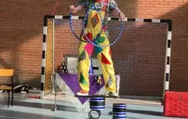 Mężczyzna w kolorowym stroju stoi na konstrukcji cyrkowej i trzyma hula hop