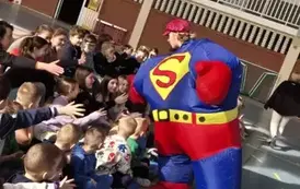Mężczyzna w napompowanym stroju Supermana wita się z dziećmi