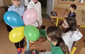 Chłopcy częstują cukierkami dwie dziewczynki, kt&oacute;re siedzą w ławce szkolnej