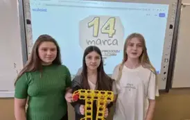 Trzy dziewczynki stoją przed tablicą multimedialną z liczbą Pi zbudowaną z klock&oacute;w reko