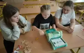 Dziewczynki siedzą przy stole i wycinają elementy do kartek wielkanocnych