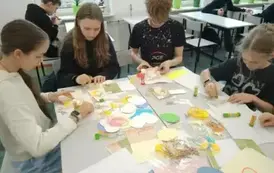 Uczniowie siedzący przy stole wykonujące kartki wielkanocne.