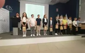 Dzieci stojące w rzędzie trzymają torby z nagrodami