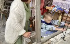 Pani stoi obok chłopca, kt&oacute;ry pracuje na krosnach