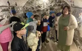 Gromadka dzieci stoi w piwnicy i patrzy na panią, kt&oacute;ra opowiada o kolekcji czarownic