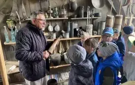 Gromadka dzieci stoi bokiem i patrzy na pana, kt&oacute;ry opowiada o eksponatach z muzeum etnograficznego