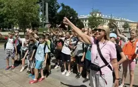 Grupa uczni&oacute;w z panią przewodnik machaja  do portalu