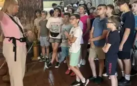 Uczniowie stoją i słuchają wykładu pani przewodnik