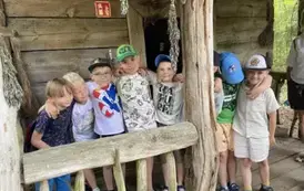 Chłopcy stoją w rzędzie za barierką przed wejściem do starej chatki