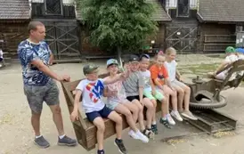 Sześcioro dzieci obok siebie siedzi na wielkiej karuzeli. Tata je kręci