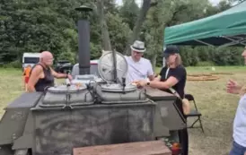 Dw&oacute;ch mężczyzn i kobieta stoją przy kuchni polowej